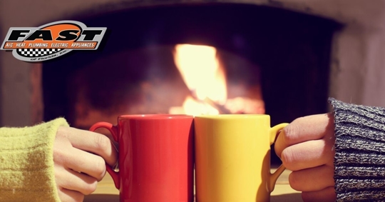 Photo of two people touching their drinking mugs together in front of a fireplace