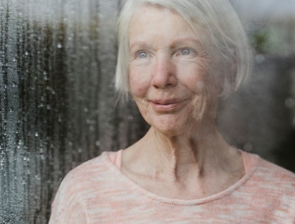 older woman looking out foggy wet window