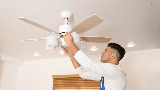 A Man Adjusts His Living Room Ceiling Fan